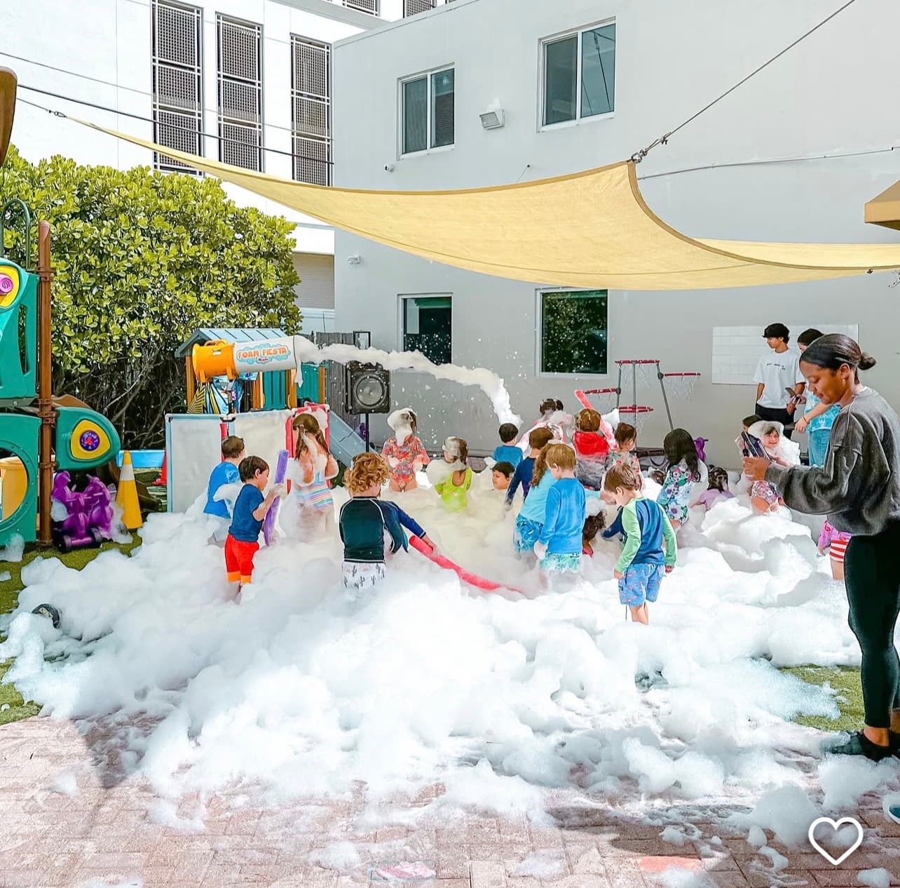Young children playing in a large pile of white foam at an outdoor playground.