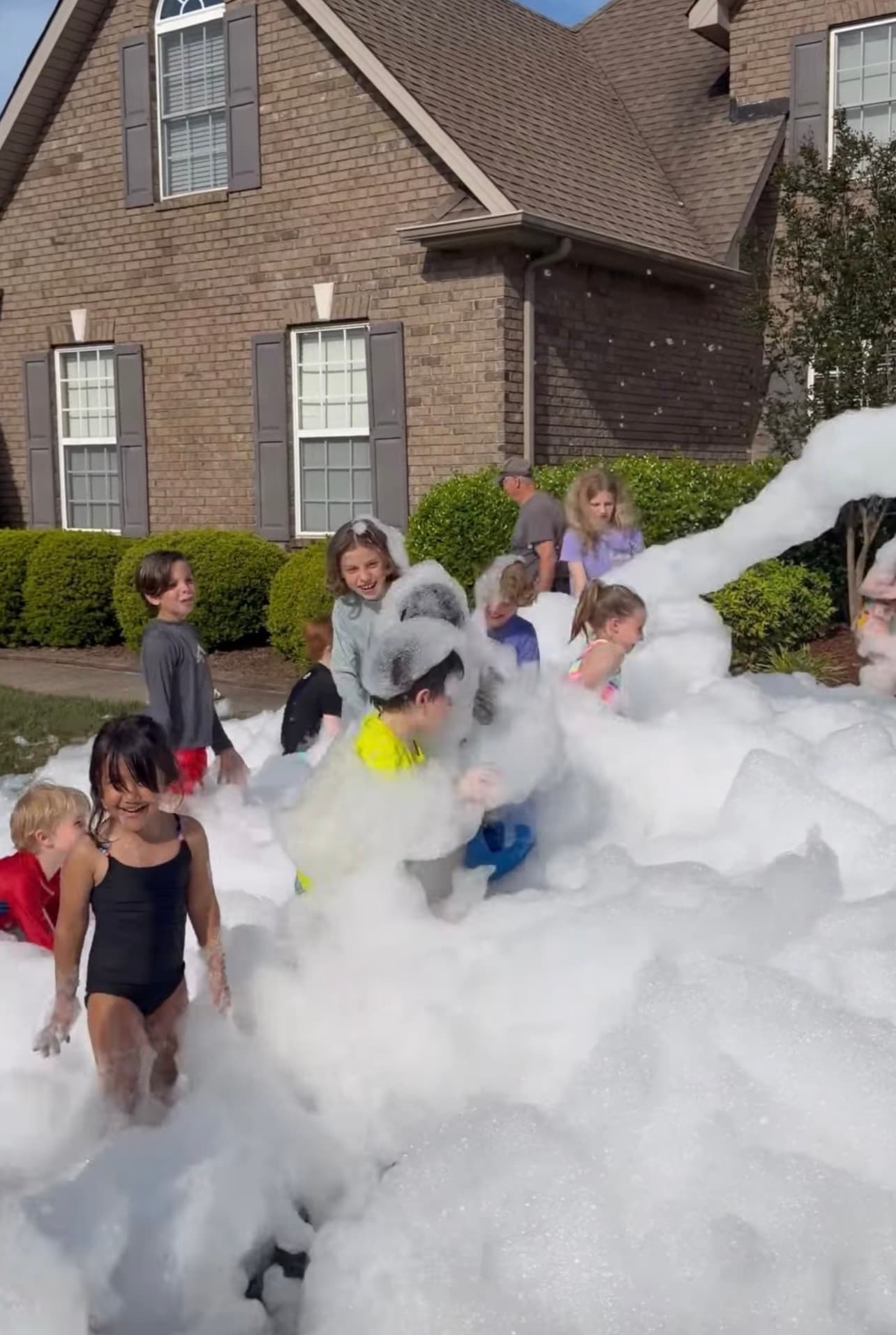 Children laughing and playing in a massive pile of white foam outside a brick house.