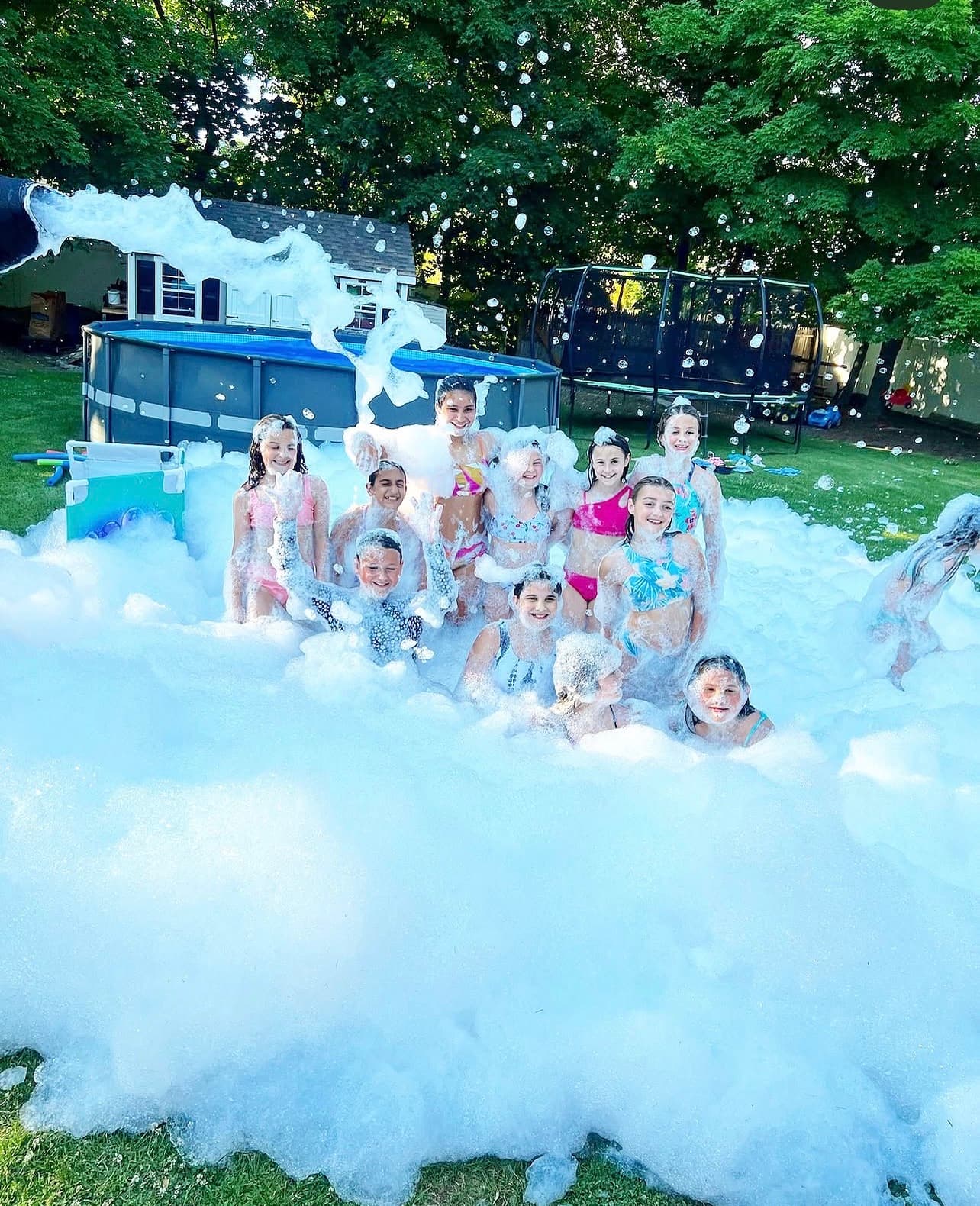 Smiling children playing in a massive pile of white foam at a backyard foam party.